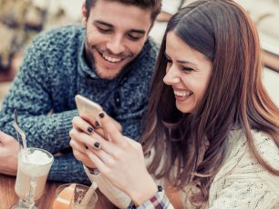 a man and woman sitting at a table looking at a cell phone.